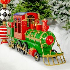 a green and red toy train sitting on top of snow next to christmas tree decorations