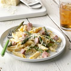 a plate of pasta with ham and asparagus next to a glass of tea