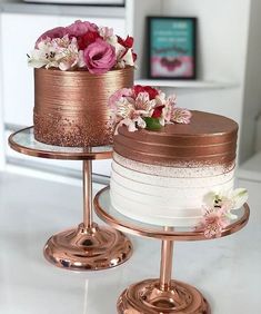 two tiered cakes with pink and white flowers on each one, sitting on gold pedestals