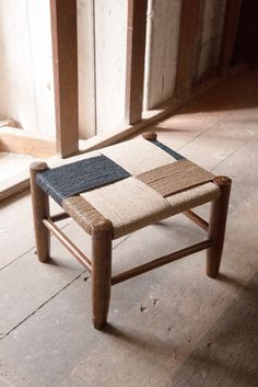 a small wooden stool with woven seat padding on the top and bottom, sitting in an unfinished room