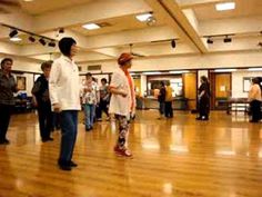 several people are standing in a large room with wood floors and hard wood flooring