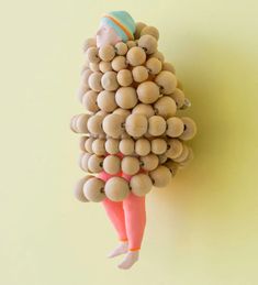 a person made out of wooden balls and wood beads on a yellow background with a pink outfit