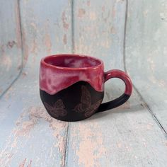 a red and black coffee cup sitting on top of a wooden table next to a wall