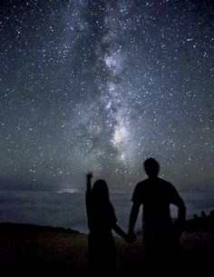 two people looking up at the stars in the night sky with their arms outstretched to each other