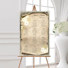 an easel with a wedding seating chart on it in front of a white vase