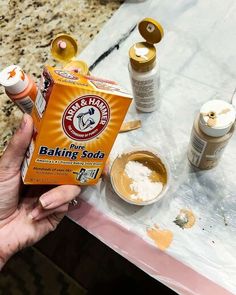 someone holding up a box of baking soda next to some other items on a table