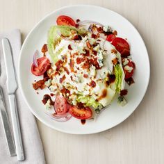 a white plate topped with lettuce, tomatoes and bacon next to a fork