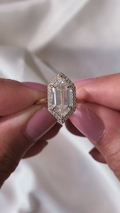 a woman's hand holding an engagement ring in front of her face with the diamond on it