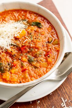 a white bowl filled with soup on top of a wooden table next to a spoon