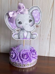 an elephant cake topper with purple flowers on a wooden table next to a cupcake