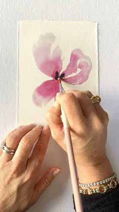 a woman is painting a flower with watercolors on white paper and holding a pencil