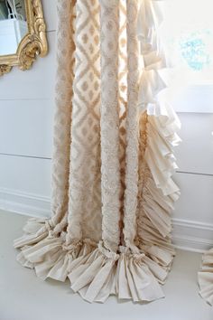 curtains with ruffles hanging from them in front of a mirror on the wall