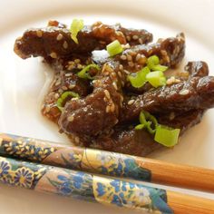 two chopsticks are sitting on a plate with meat and sesame seed sauce in it