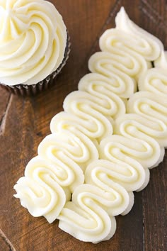 two cupcakes with white frosting sitting on top of a wooden table