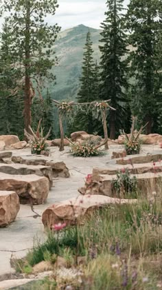 an outdoor seating area with large rocks and flowers in the foreground, surrounded by pine trees