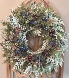 a wreath with pine cones and blue berries hanging on a wall in front of a door