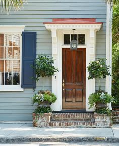 a house with blue shutters and red door on the front porch is decorated with potted plants