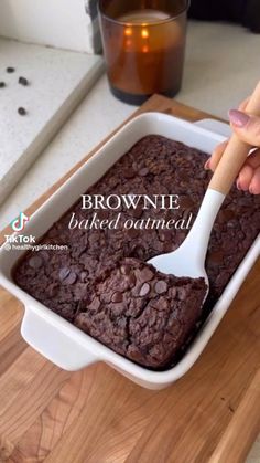 a person is spooning chocolate cake into a baking dish on a wooden cutting board