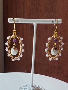 A Bead Habit very proudly presents a pair of fabulous gemstone oval earrings set in Golden toned Brass. Earring wires are made of golden Stainless Steel. Set with Natural Amethyst, Lepidolite and Moonstone gemstones, these oval earrings make a bold yet feminine statement. The center dangle is made of natural Howlite. Earrings are approximately 40mm Tall including the earring wire. These Boho style earrings are made with a wire wrapping technique. The Moonstones are faceted and are associated wit Gold Oval Jewelry With Gemstone Beads, Unique Oval Faceted Beads Jewelry, Adjustable Gemstone Briolette Earrings, Handmade Oval Moonstone Earrings, Oval Amethyst Earrings With Gemstone Accents, Chip Jewelry, Howlite Earrings, Moonstone Gemstones, Wire Wrapping Techniques