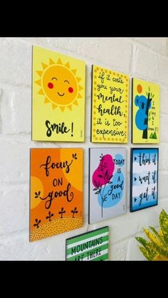 four colorful paintings hanging on the wall in front of a white brick wall, each with different sayings