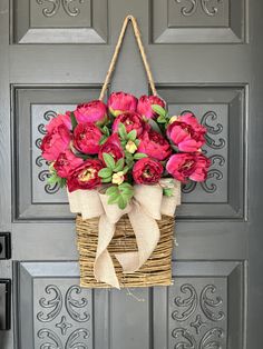 a basket filled with pink flowers hanging from a front door hang on a gray door