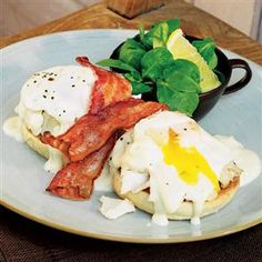 an english muffin topped with bacon and eggs on a plate next to a bowl of spinach