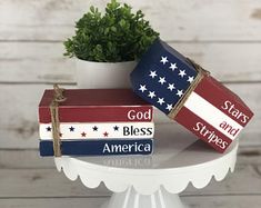 three patriotic books tied to each other on top of a white pedestal with a potted plant in the middle