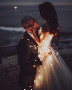 a bride and groom standing next to each other in front of the ocean at night