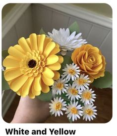 a hand holding a bouquet of flowers with yellow and white flowers in it's center