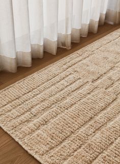 a beige area rug on the floor next to a window with white drapes and curtains