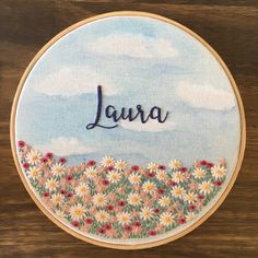 a hand embroidered wall hanging with flowers and the word'laura'in cursive writing