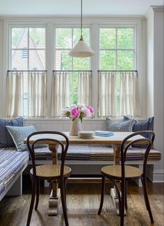 a dining room table with two chairs and a bench in front of the bay window