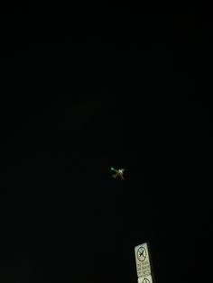 an airplane is flying in the dark sky above a street sign and traffic light at night