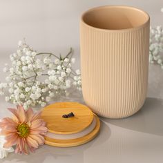 a white vase sitting next to a pink flower and a wooden coaster on a table