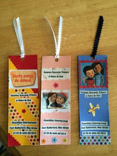 two bookmarks with children's pictures hanging from them on a wooden table next to a pair of scissors