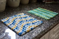 two crocheted squares are sitting on the counter next to each other in front of coffee mugs