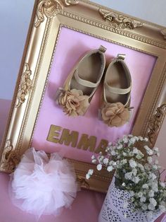 there is a framed picture with baby shoes and a flower pot on the table next to it