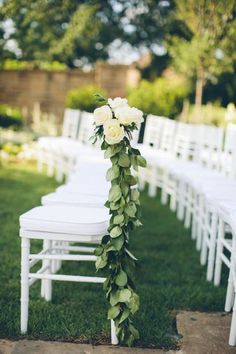 white chairs are lined up with flowers and greenery on the back of each chair