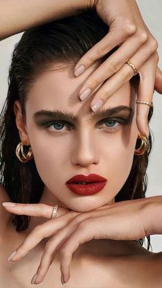 a woman with red lipstick and gold rings on her head, holding her hands to her face