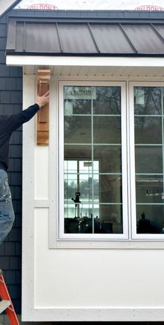 a man on a ladder painting the side of a house with windows and sidings