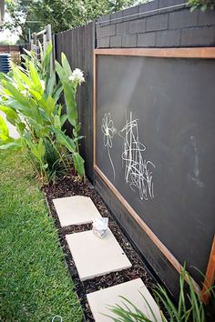 a blackboard in the middle of a garden with stepping stones and plants around it