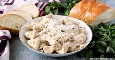 a white bowl filled with chicken salad next to bread and parsley on a table