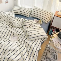 there is a bed with blue and white striped sheets on the floor next to a laptop