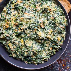 a bowl filled with spinach and cheese on top of a table next to bread