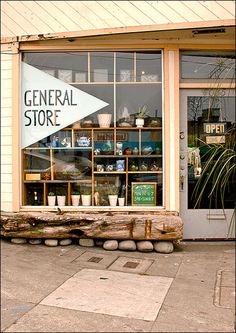 a store front with an arrow sign in the window and potted plants behind it