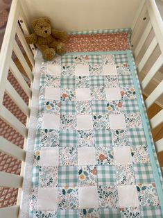 a teddy bear sitting on top of a crib next to a quilted blanket