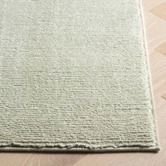 a light green rug on the floor with wood floors in the background and an area rug that has been made to look like woven fabric