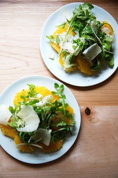 two white plates topped with salad on top of a wooden table