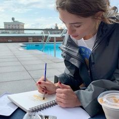 a woman sitting at a table with a notebook and pen in her hand while writing