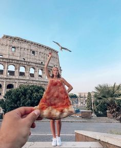 a woman holding up a slice of pizza in front of the colossion with a bird flying above her